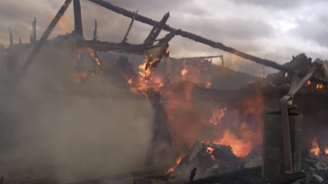 Zoom-in past fireman in foreground to flaming ruins of a burned house