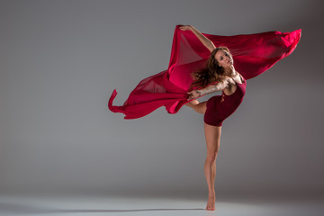 Beautiful woman dancer wearing maroon swimsuit posing on a grey studio background