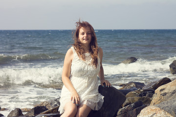 beautiful young woman sitting on stone against the sea