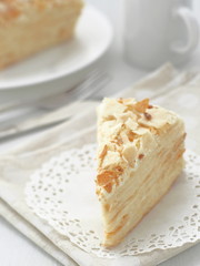 Piece of multi layered cake close-up. Mille feuille dessert. Crumbs decorated torte on white doily upon wooden table. Food background, blur. Selective focus on the front.