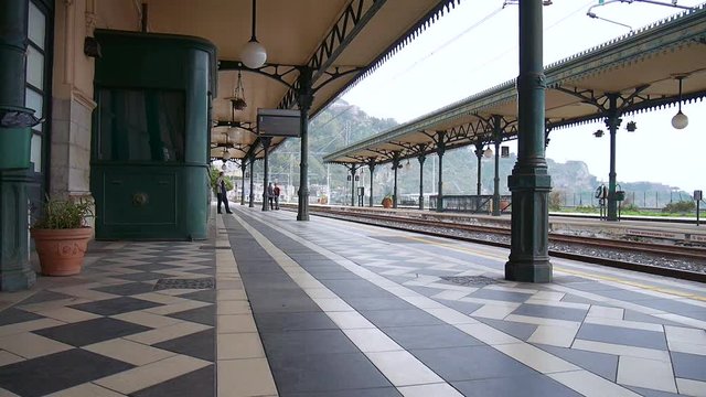 Fixed shot of people waiting in the train station of Taormina, Italy on a cloudy sunny day