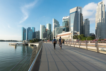 Pedestrians walk along bridge near Marina bay in Singapore with Singapore skyscraper and Merlion...