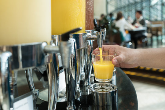 Hand holding glass refill orange juice for row of fresh juice at buffet restaurant, Juice buffet self service in morning at hotel.