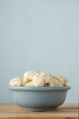 Bowl of Raw Cauliflower Florets on Wood Plank Table with Blue Background
