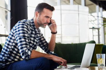 Man at cafe talking on the phone and using his laptop
