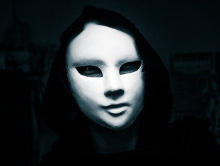 Artistic, monochrome picture of a white carnival mask weared by a woman in darc clothes