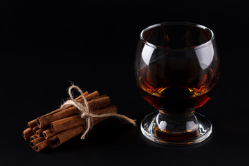 Glass of cognac or dark rum and cinnamon sticks on black background