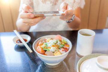 Obraz na płótnie Canvas Woman’s hands taking picture of Japanese sashimi dish by smartphone camera, soft-focus on hand and defocus in background.
