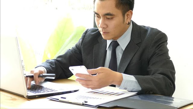 Businessman at desk using smart phone and laptop computer and working on reports