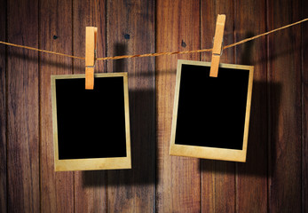 Old picture frame hanging on clothesline on wood background.