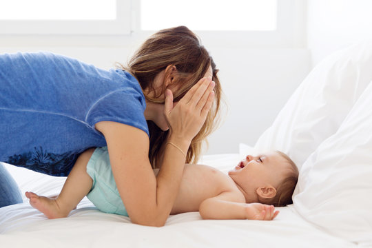 mother and baby playing peek-a-boo on the bed and laughing