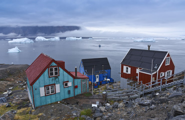 colored houses in front of icebergs at the shore of umanak in greenland