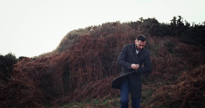 Man walks into frame and stands, looking out over vast ocean and cloudy sky in Ireland, model released. 4k
