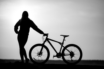 Fototapeta na wymiar Shadow of srorty slim woman in sportswear near her bicycle on a road at sunset
