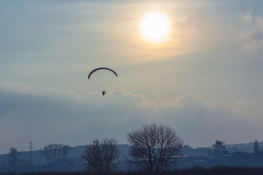 paramotor glider flying in the sky over beautiful countryside field landscape
