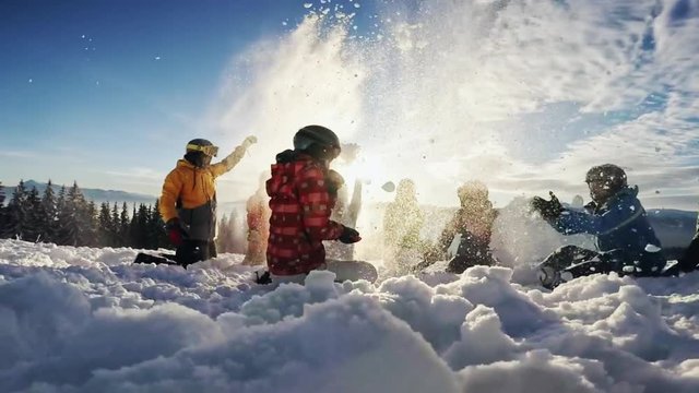 Happy groupof skiers having fun sitting in snowdrift with snowboards and tossing snow
