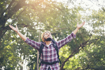 Handsome man (bag packer) wearing a striped shirts and outstretched hands,happy face and smiling.He stood in the middle of the woods.