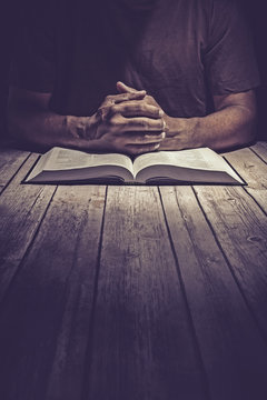 Man Praying On A Wooden Table With An Open Bible