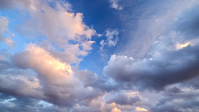 Time-lapse footage of blue sky full of golden clouds during colorful sunset.