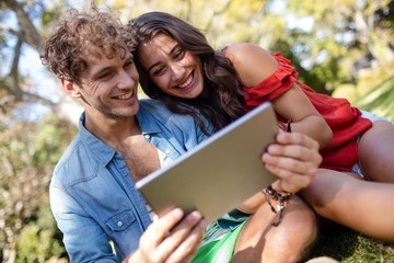 Couple sitting on grass and using digital tablet