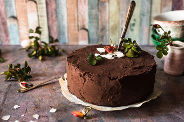 torta vegana al cioccolato fondente e cocco con coltello per il taglio di una fetta; piccoli boccioli di rosa e ciotole su sfondo rustico