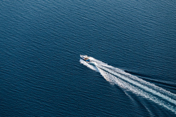 Top view of a small boat floating in the sea and creates a white waves.