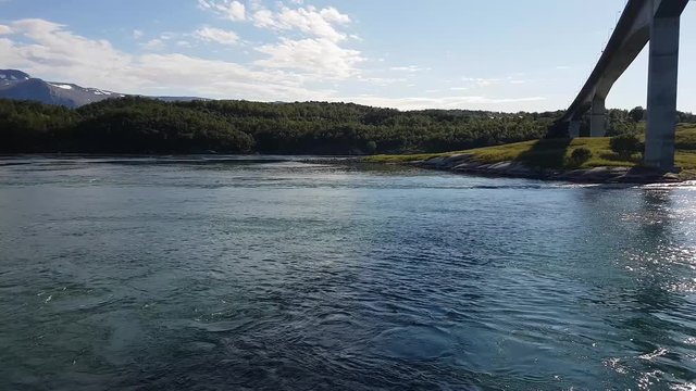 Yacht sailing under bridge. in strait with water boiling in tidal current. Saltstraumen, Bodo, Norway.