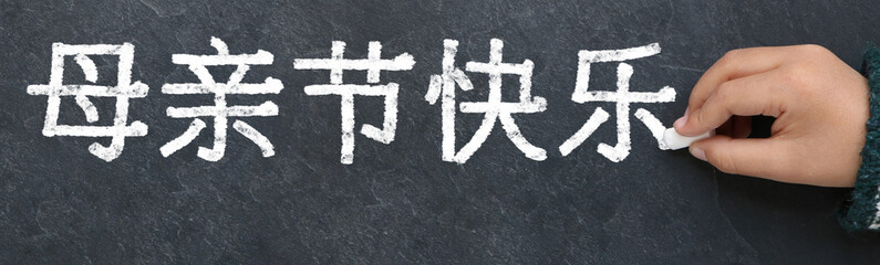 Enfant écrivant bonne fête des mères en chinois à la craie sur une ardoise
