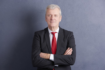 Confident senior businessman standing against grey wall