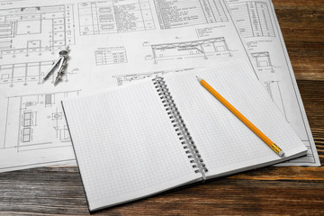 Open blueprints on wooden table background with a pencil and compasses lying beside.