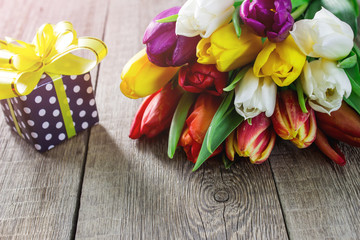 Bouquet of colorful tulips and gift box on wooden table