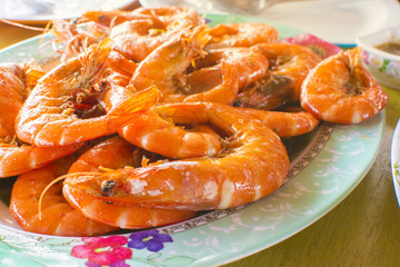 Baked salt prawns in bowl on a wooden table with selective focus.