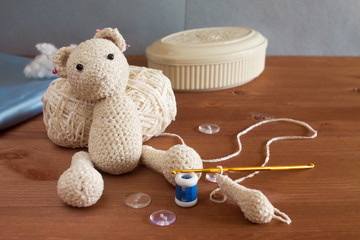 Crochet toy bear in the process with accessories and materials: yarn, hook, row counter