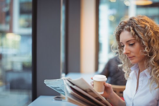 Woman reading newspaper while having coffee