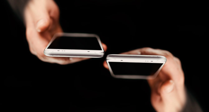 Horizontal view of modern phone, technology concept. Two mens holding phones versus each other in hands, with black background