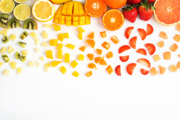 Top view of red, orange, yellow, green fruits with cut pieces on the white background; grapefruit, mango, strawberries, orange, lemon, kiwi