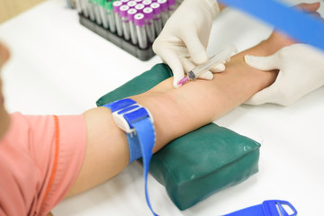 Laboratory with nurse collecting a blood sample from patient, in background blood test tubes.