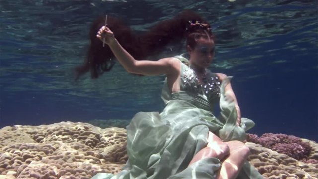 Young girl model underwater poses for camera on background of corals in Red Sea. Filming a movie. Extreme sport in marine landscape, coral reefs, ocean inhabitants.