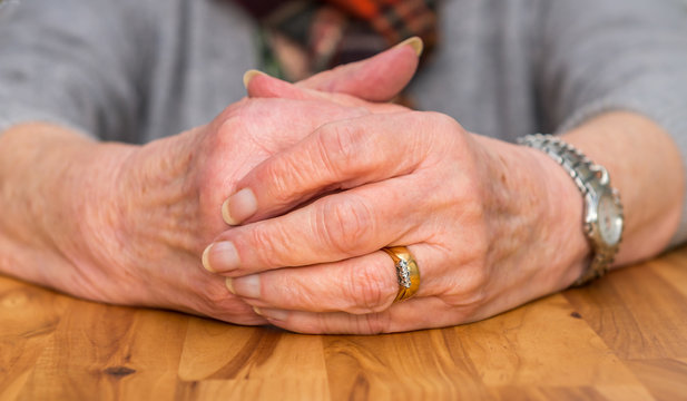 Clasped hands of a female pensioner resting on a table.
