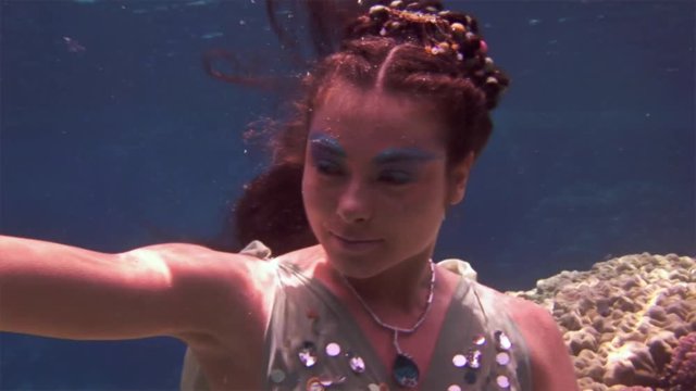Underwater model free diver swims in clean transparent blue water in Red Sea. Filming a movie. Young girl smiling at camera. Extreme sport in marine landscape, coral reefs, ocean inhabitants.