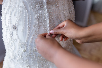 bridesmaid buttoning the wedding dress of the bride