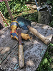 Garden hand trowel, hose sprayer head and an old flower rake in the summer garden