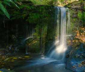 Fototapeta na wymiar Small waterfall over a mossy stone wall