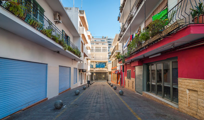 Fototapeta na wymiar Vacant & shaded, empty alleyway on otherwise bright sunlit day in Sant Antoni De Portmany. Ibiza in quiet off-season in the afternoon. 
