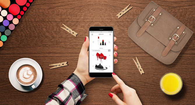 Women shopping shoes online, holding modern phone in hands on table with bag, coffee, and makeup beside