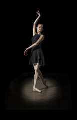 Young and incredibly beautiful ballerina is posing in darkness hall on parquet.