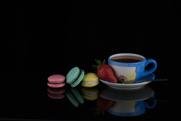 A cup of tea with strawberries and colorful macaroons on a black background