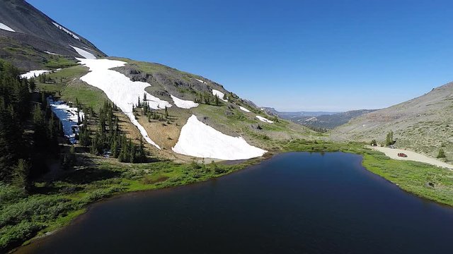 4k UHD Aerial tracking back from snow capped mountain with calm mountain lake below in Arnold California in the Yosemite National Park as camera tracks away from mountain
