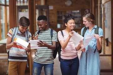 Happy classmates looking at grade cards in corridor