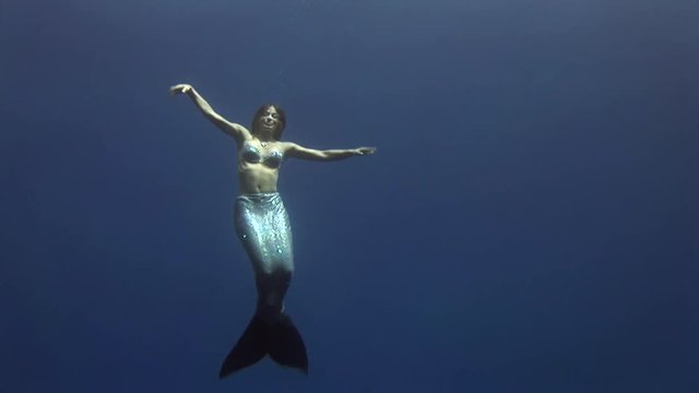 Young girl model underwater mermaid costume on blue background poses in Red Sea. Filming a movie at camera. Extreme sport in marine landscape, coral reefs, ocean inhabitants.